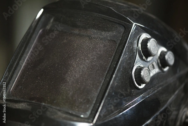 Obraz Protective welding mask visor with adjustment knobs showing worn transparent screen on industrial workshop background.