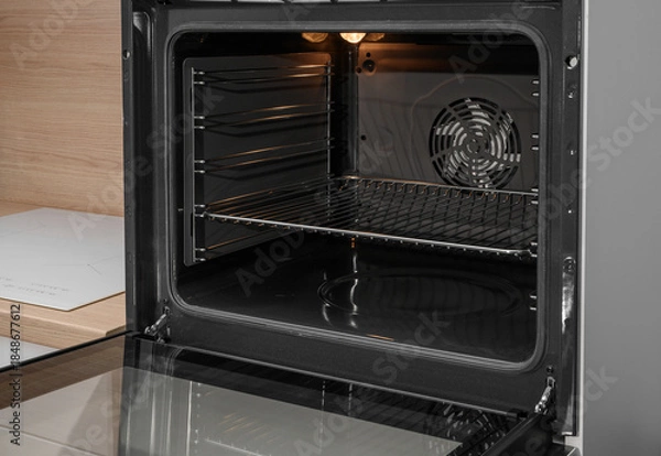 Obraz An open, empty oven at home, with a grate inside and the light on.