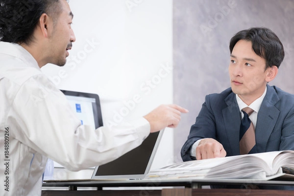 Fototapeta 作業着の男性とスーツの男性が内装工事や施工など打ち合わせをする　言ってること契約と違う…？とクレームを入れる