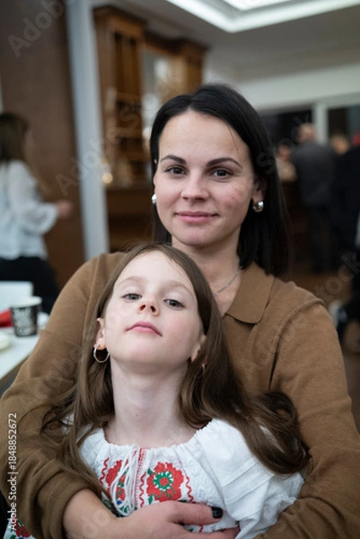 Fototapeta Vertical photo of affectionate middle aged mother and her daughter in vyshyvanka, emotional family bond concept