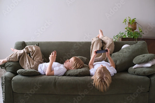 Fototapeta kids boys twins using smartphones lying on the couch