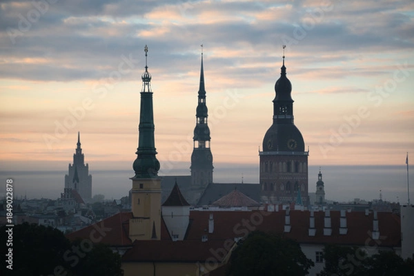 Fototapeta Blick über die Dächer von Riga in Lettland in der dunstigen Morgendämmerung mit den Turmspitzen mehrerer Kirchen in den Silhouetten