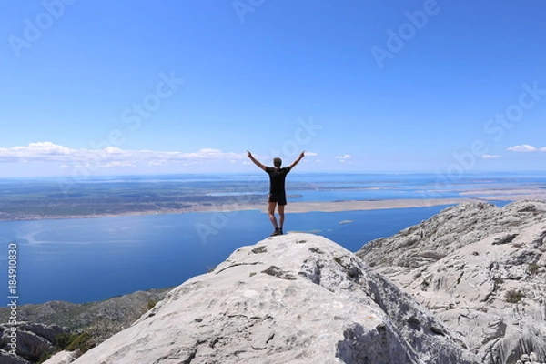 Fototapeta Silhouette of happy man standing on rock and arms outstretched against the sky