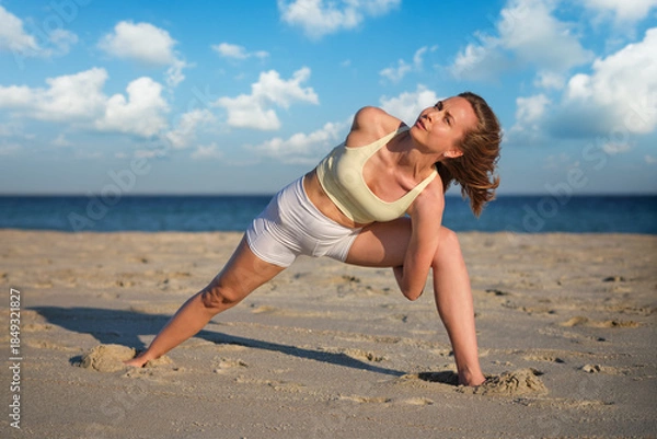 Obraz Woman performs bound triangle pose on beach during sunset