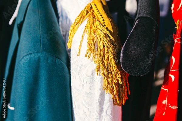 Obraz Assorted garments hanging together, teal jacket shoulder next to white textured dress or garment adorned with a thick, golden tassel accessory. Glimpse inside a crowded theater wardrobe