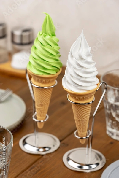 Obraz 木製テーブルのカフェに並ぶ抹茶ソフトクリームとバニラソフトクリームコーン