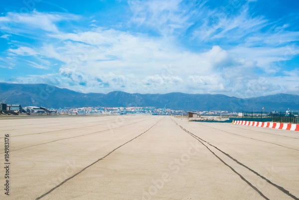 Fototapeta Beautiful landscape view of runway, airstrip in the airport terminal ready for airplane landing or taking off with blue cloudy sky and mountains at background. Travel aviation future concept.