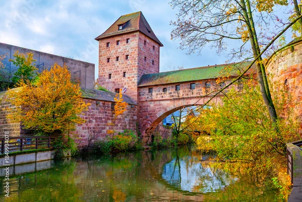 Obraz Fronveste building and part of old city wall and bridge system in Nuremberg, Germany, reflected in Pegnitz River. Autumnal scene with historic red sandstone architecture and lush surrounding foliage