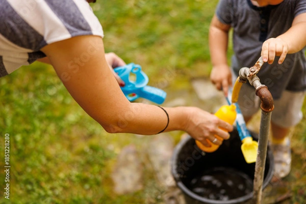 Obraz Mother and son filling toy gun with water while playing in the backyard of their home