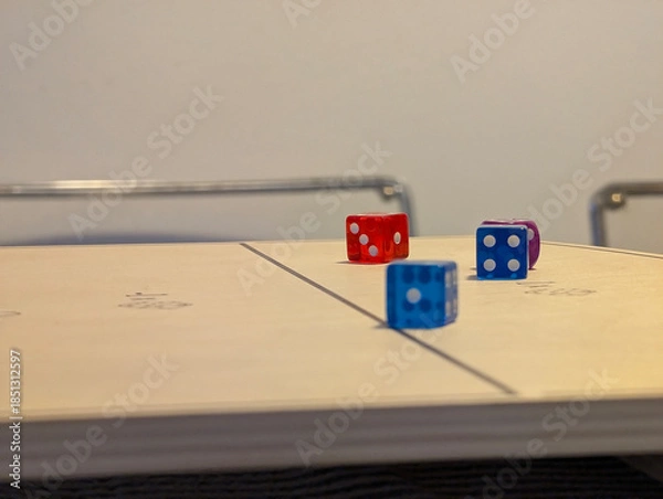 Obraz Low-angle perspective of colorful translucent dice on wooden board of tabletop game. Leisure, hobby, dexterity, physics-based, strategy, rolling, scoring, numbers, pips, entertainment, indoor activity