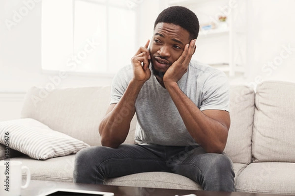 Fototapeta Sad young man talking on mobile at home