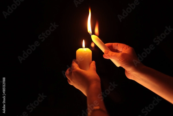 Fototapeta Hands holding burning candle in black dark. Selective soft focus, blur smoke light and shadow contrast background.