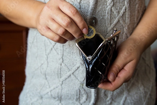 Fototapeta The woman holds the coins over the old empty wallet. The concept of poverty