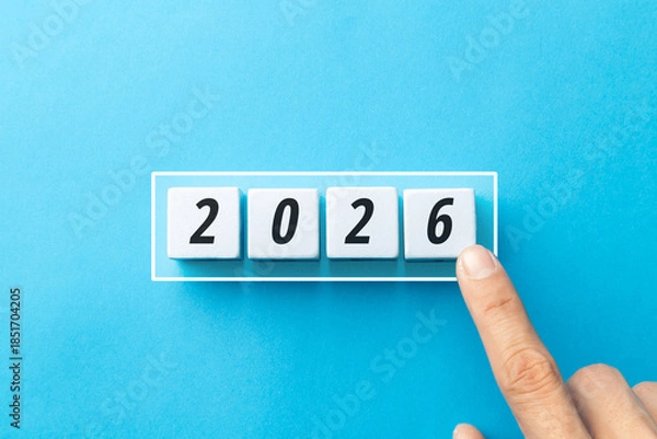Fototapeta Minimalist concept of transition to 2026 with white cubes on a blue background. Features loading bar, finger touching block, and flipping 2025 to 2026 to represent future goals and business planning.
