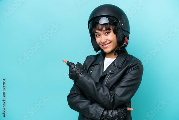 Obraz Young Argentinian woman with a motorcycle helmet isolated on blue background pointing finger to the side