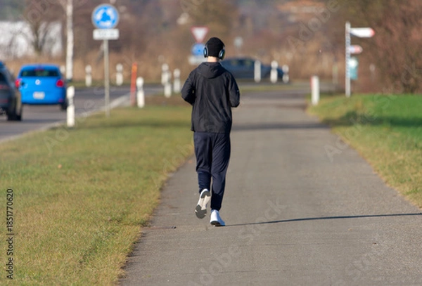 Obraz Rear view of young man with cap and headphones at Swiss village of Niederglatt on a sunny autumn afternoon. Photo taken December 20th, 2025, Niederglatt, Canton of Zurich, Switzerland.