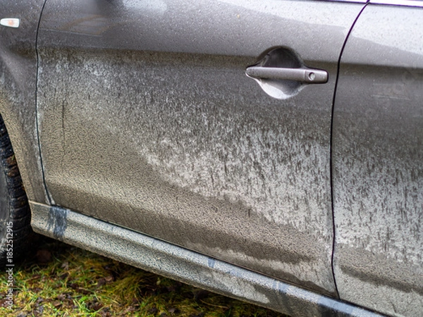 Fototapeta A car covered in mud. Autumn, winter and spring mud on the roads. Car wash services. Side view of a very dirty car