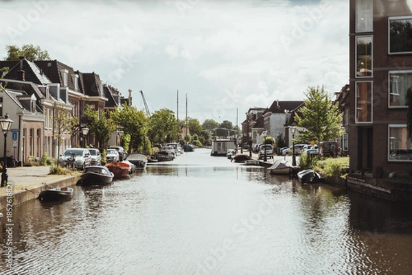 Fototapeta The beautiful canals of Leiden city centre surrounded by buildings, Dutch houses and boats along the water outdoor at daytime during summer in Leiden in The Netherlands with space for text.