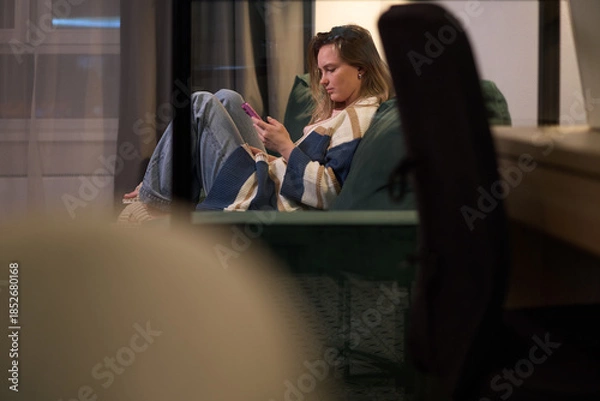 Obraz Female sitting on sofa using smartphone indoors