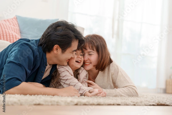 Fototapeta Happy Asian family lying on carpet at home father and mother hugging laughing daughter with love and warmth in cozy living room
