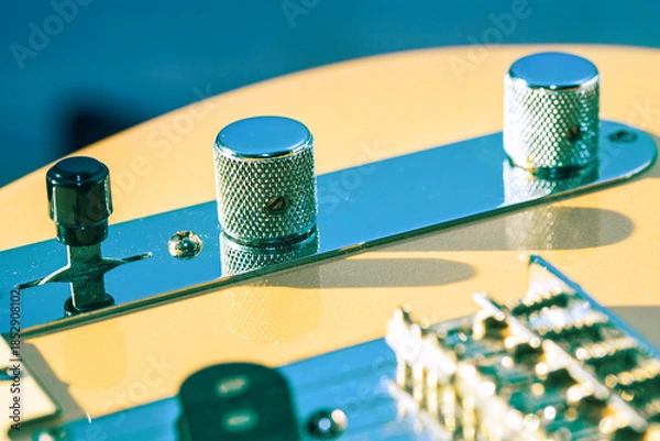 Obraz Classic electric guitar control plate showing chrome knobs and black switch against wood body. Metal components reflect blue light, highlighting instrument vintage aesthetic and hardware details