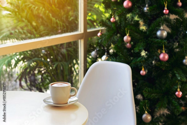 Obraz Embracing holiday spirit with delicious hot cappuccino on table near window and beautiful view of decorated Christmas tree in background. hot cup of coffee with Merry Christmas festive decorations.