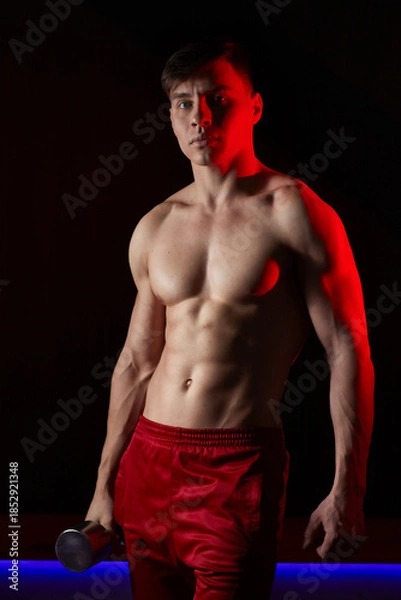 Fototapeta Young man posing with dumbbell in dramatic lighting