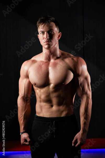 Fototapeta Portrait of a sweaty muscular bodybuilder posing on black background.