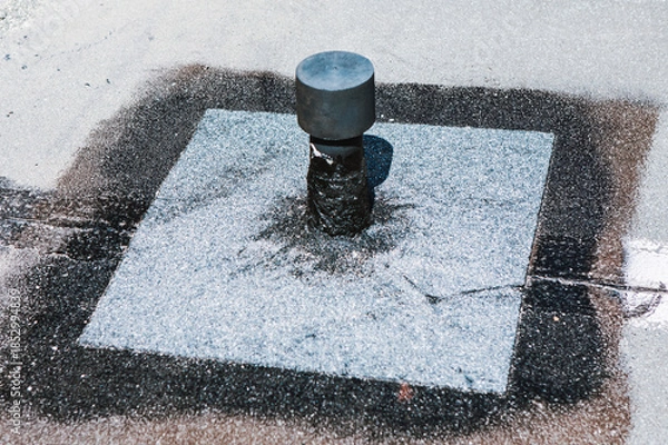 Obraz Flat roof vent is installed on a rooftop. Seal looks effective around the base. Bitumen roof penetration flashing detail, showing granular surfacing