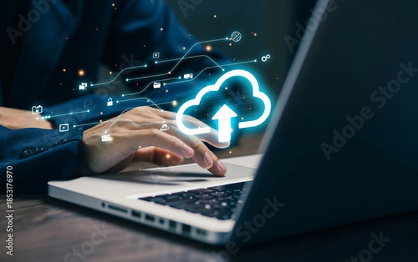 Obraz A professional uses a laptop with a glowing cloud upload icon, representing cloud computing, data storage, file synchronization, digital transformation, and secure online infrastructure.