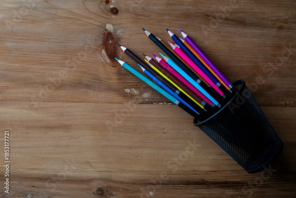 Obraz Top view of colored pencils in fallen pen holder on wooden desk.