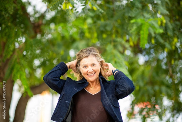 Obraz Joyful woman adjusting hair while standing under vibrant green tree