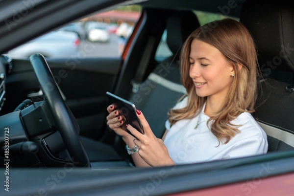 Obraz Young woman drives car and uses portable touchscreen computer