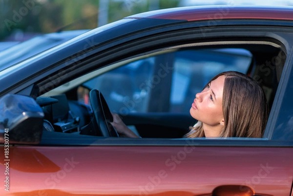 Obraz Young woman looks at the sky from her car, checking the weather
