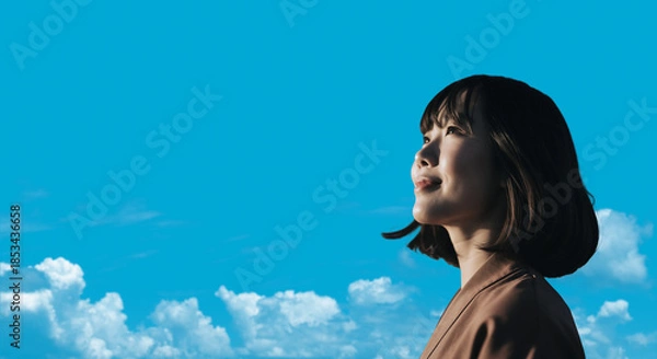 Obraz 春・上を見上げ微笑む明るい表情の日本人女性の顔　前向きでポジティブ希望に満ちた表情　就職・新生活・旅行・リラックス・入学のイメージ　青空と雲の背景