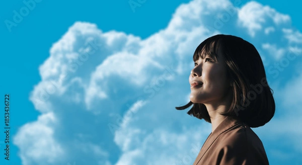 Obraz 春・上を見上げ微笑む明るい表情の日本人女性の顔　前向きでポジティブ希望に満ちた表情　就職・新生活・旅行・リラックス・入学のイメージ　青空と雲の背景