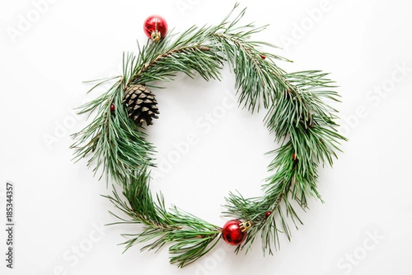 Fototapeta Traditional Christmas wreath from a green pine tree with red balls on a white background, flat, top view
