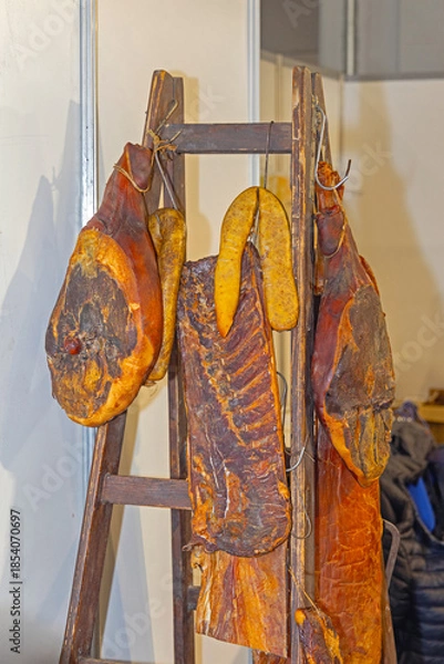 Fototapeta Dry Delicatessen Cured Meat Dried Ham Slab of Bacon Hanging at Wooden Ladder