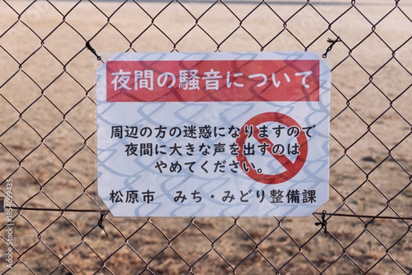 Obraz 松原市民運動広場の夜間騒音警告：逆光で金網の影が文字に重なる「通行止め」マーク入りの看板