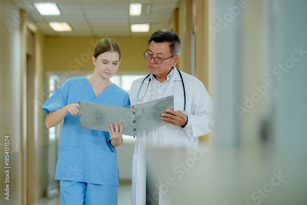 Fototapeta doctor and a nurse standing together in a hospital corridor, reviewing medical documents on a clipboard.