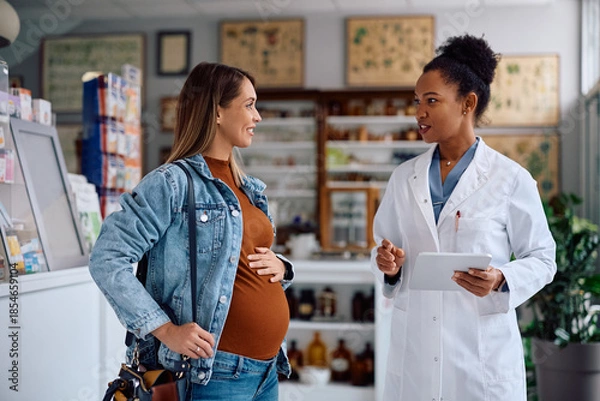 Obraz Happy pregnant woman consulting with pharmacist in drugstore.