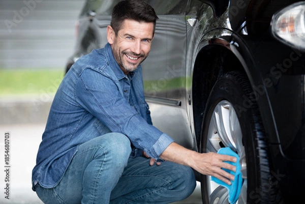 Obraz man cleaning automobile wheel with duster closeup