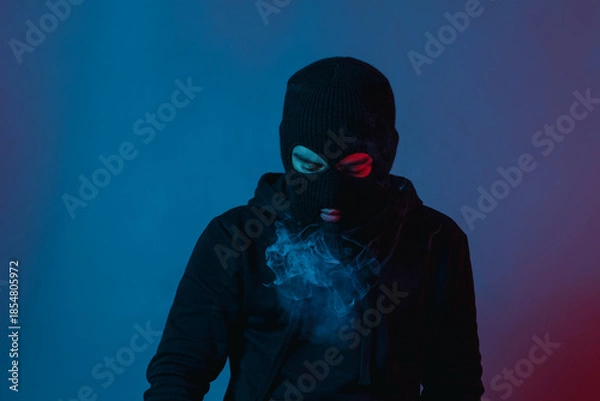 Fototapeta man in hoodie and balaclava looking down and blow smoke out