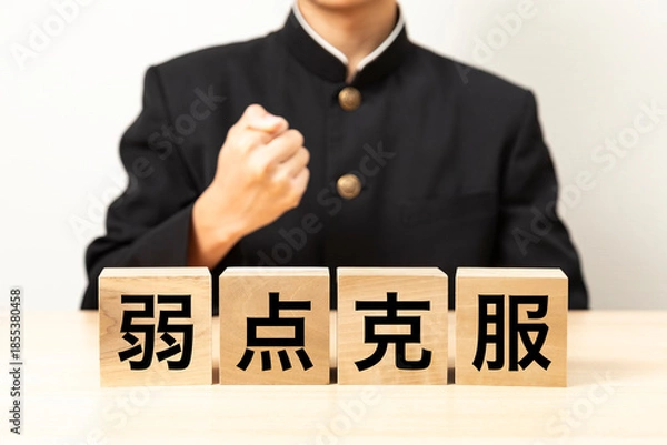 Obraz 「弱点克服」と書かれたブロックとガッツポーズをする男子学生