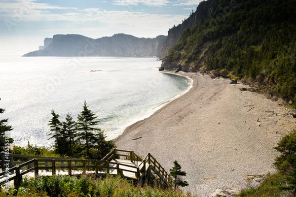 Fototapeta A walkway leading down to a beautiful beach with blue water and green trees on the surrounding mountainous landscape