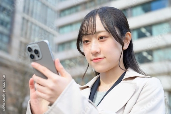 Fototapeta ビル街でスマホを使用する日本人ビジネスウーマン