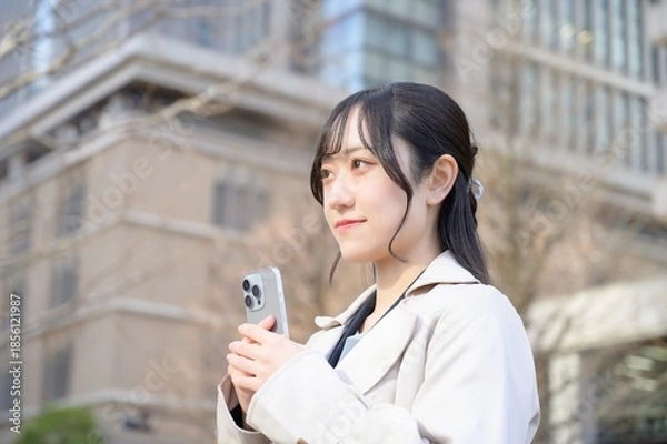 Fototapeta ビル街でスマホを使用する日本人ビジネスウーマン