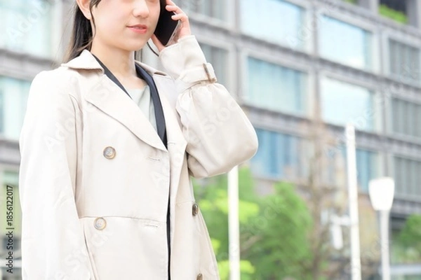 Fototapeta ビル街でスマホを使用する日本人ビジネスウーマン