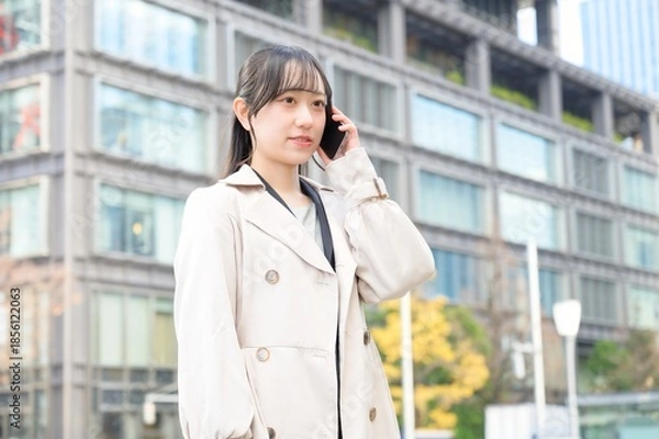 Fototapeta ビル街でスマホを使用する日本人ビジネスウーマン