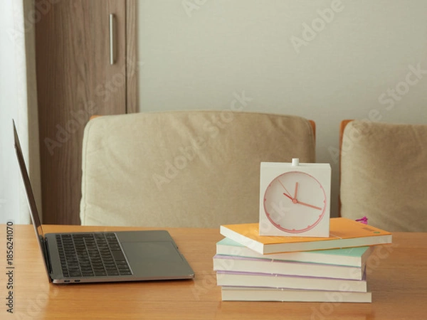 Obraz 家のリビングの机の上にあるノートパソコンと本と時計の様子
